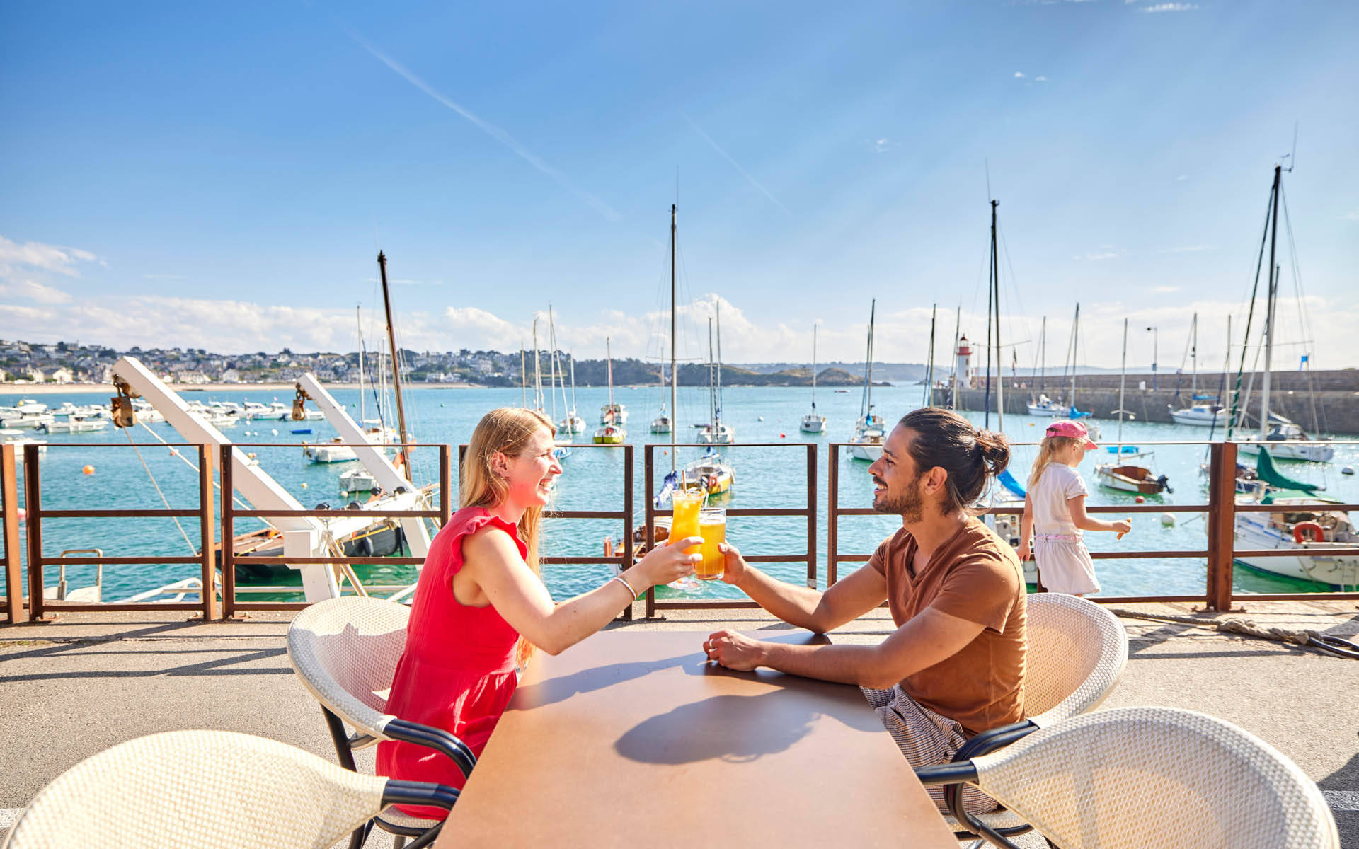 Un homme et une femme attablés en terrasse, vue sur le port d'Erquy