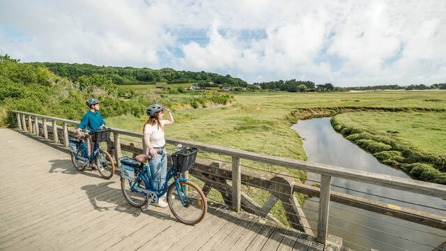 Deux cyclistes avec leurs vélos sur la passerelle des marais de plurien